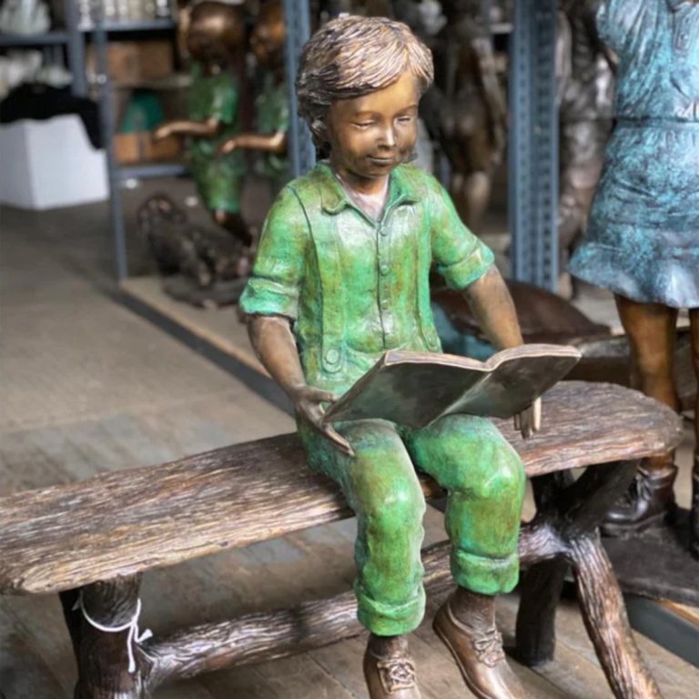 Statue eines Jungen, der auf einer Bank liest