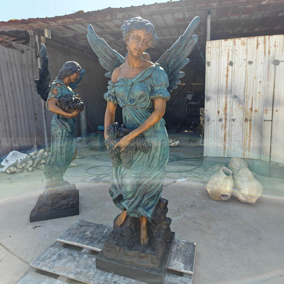 A pair of angel Angel Art Sculptures, one angel holding a bunch of grapes