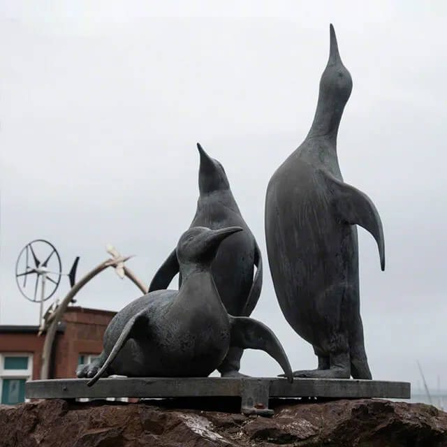 Bronzene Pinguin-Statue mit drei Kaiserpinguinen, von denen einer hoch aufrecht steht und zwei in entspannteren Positionen