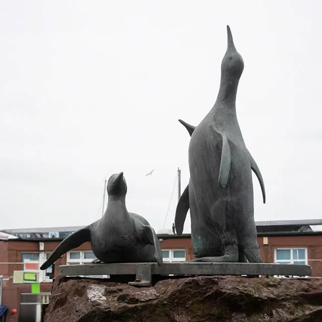 Bronzene Pinguin-Statue mit drei Kaiserpinguinen, von denen einer hoch aufrecht steht und zwei in entspannteren Positionen