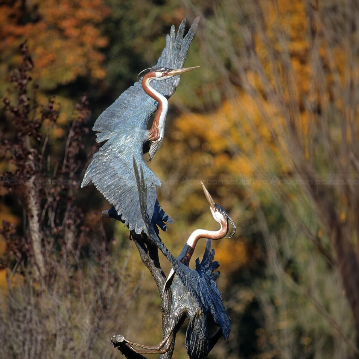 Deux sculptures extérieures de héron debout sur une branche avec les ailes entièrement déployées