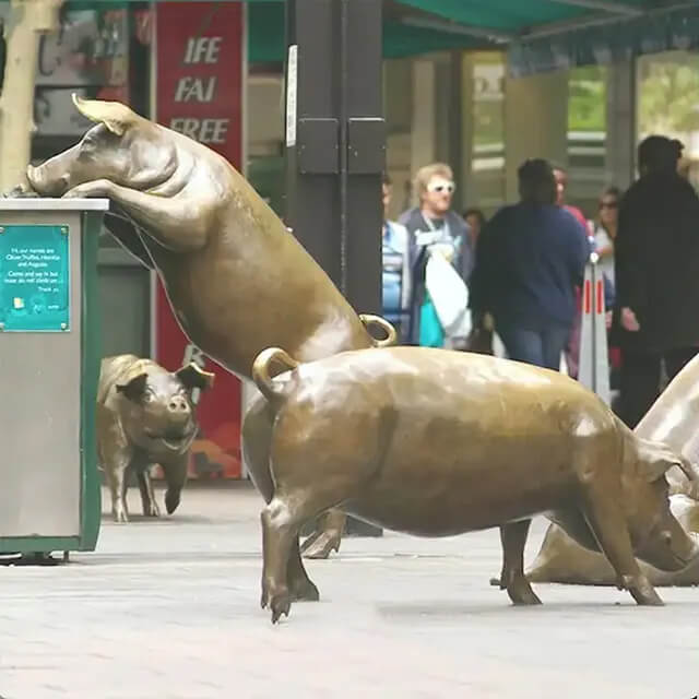 escultura de bronce A Day Out que muestra un cerdo subiendo a un cubo de basura con otros cerdos de fondo.