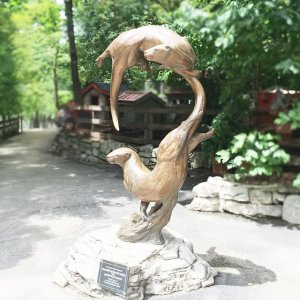 Bronzene Otter-Gartenskulptur, die zwei schwimmende Otter darstellt, eine über der anderen, beide auf denselben Punkt voraus fokussiert