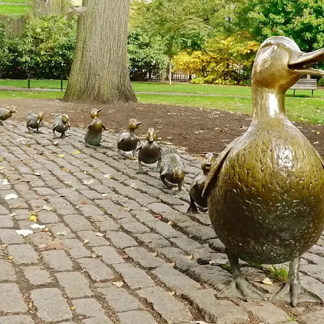 estátua em bronze de 'Dar Passagem para os Patinhos', mostrando a mãe pato com seus filhotes caminhando sobre paralelepípedos