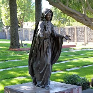 Bronzene Rasenstatue der Jungfrau Maria mit ausgebreiteten Armen auf einem Friedhof