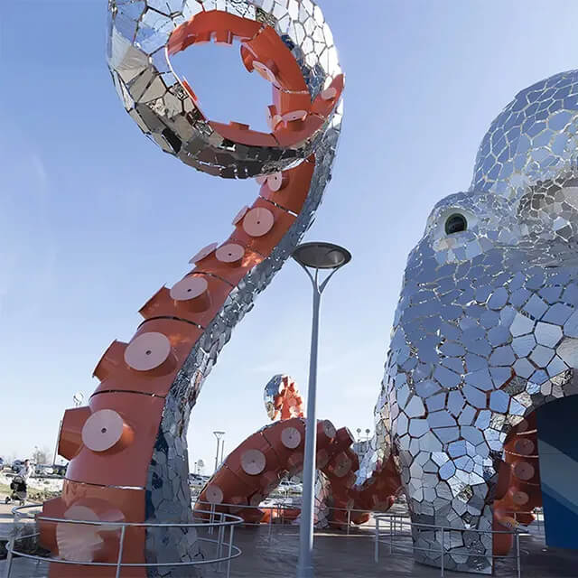 Close-up of a raised tentacle from the stainless steel Giant Octopus Sculpture with vibrant orange suction cups