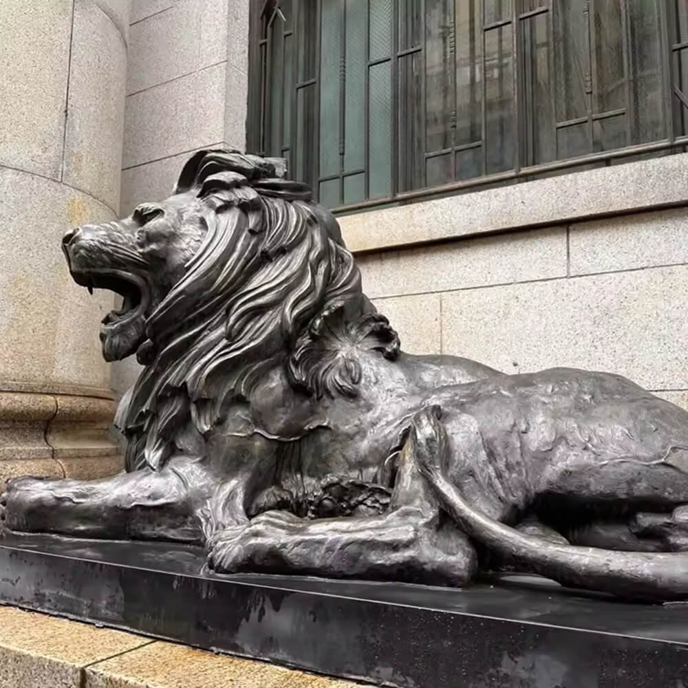 Grande statue extérieure en bronze d'un lion couché placée devant un bâtiment