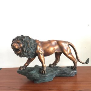 Estatua de león macho de bronce de pie sobre una base de roca con expresión rugiente