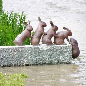Esculturas de conejos para exteriores en bronce que muestran un grupo de conejitos ayudándose mutuamente en una repisa de piedra
