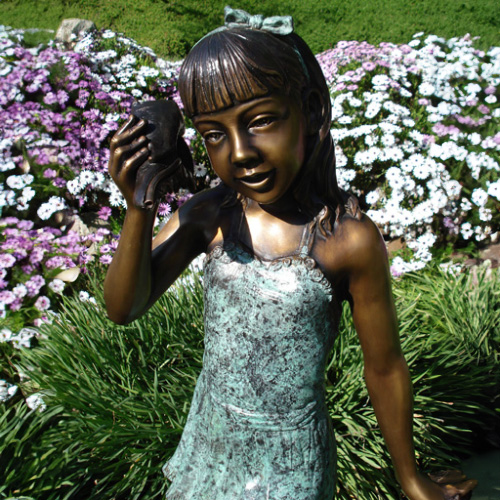 Detalle cercano de la estatua de bronce de niña escuchando una concha